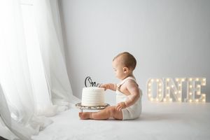 A baby in a white onesie sits next to illuminated marquee letters during a one year milestone photo session.