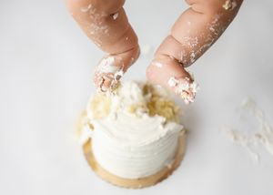 Fingers press into creamy white frosting on top of a small individual dessert with a cookie base.