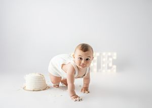 Baby in white onesie crawls on floor with illuminated letters and neutral backdrop.