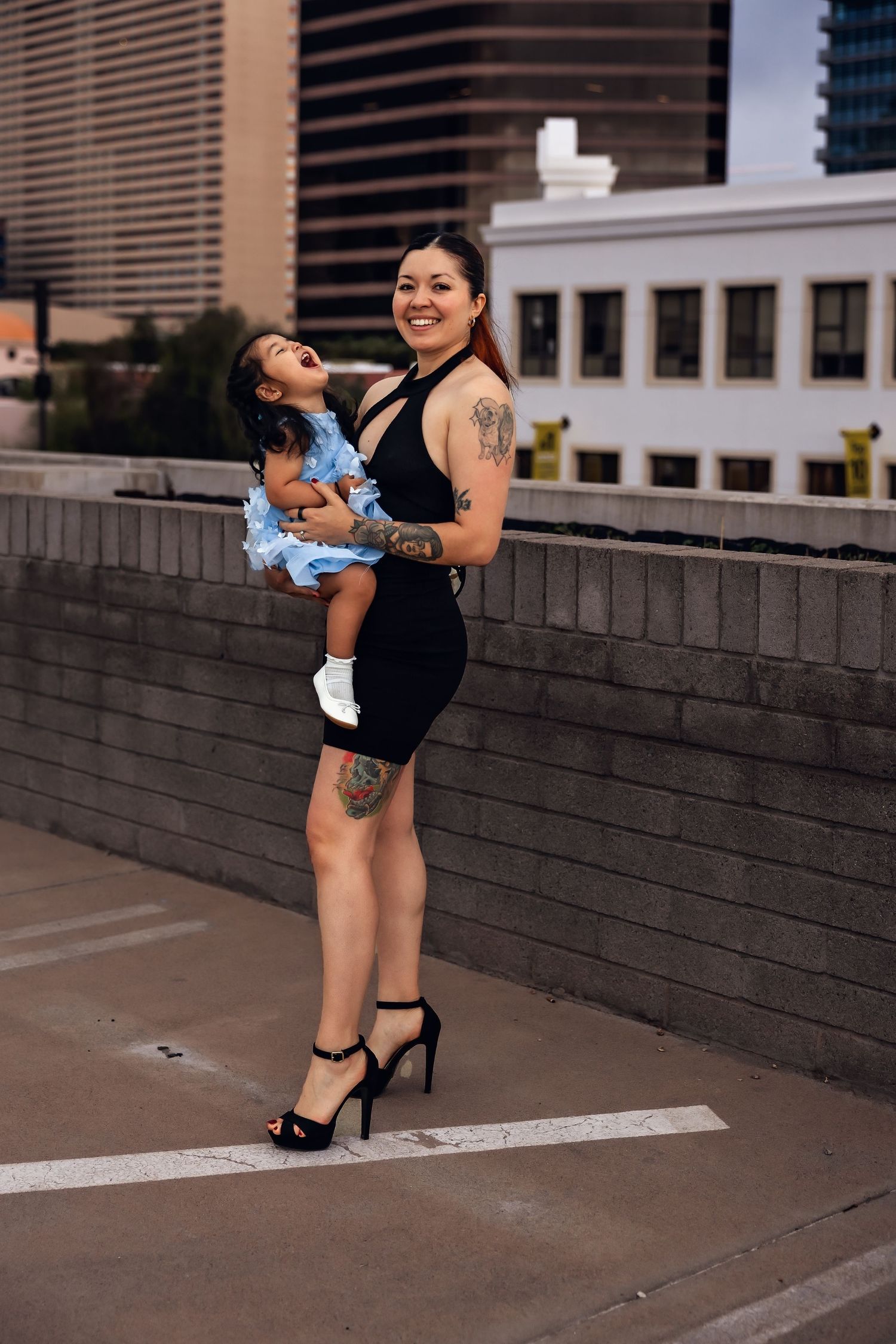 Mother and small child share a joyful moment together on an urban rooftop with city buildings in the background.