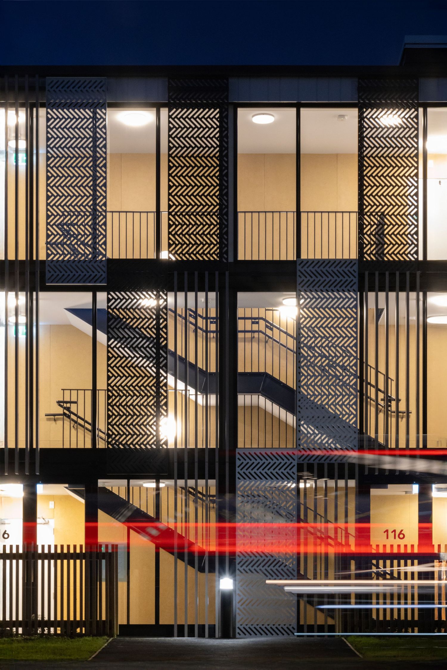 Office building at night with glowing interiors and striped façade with light trails below.