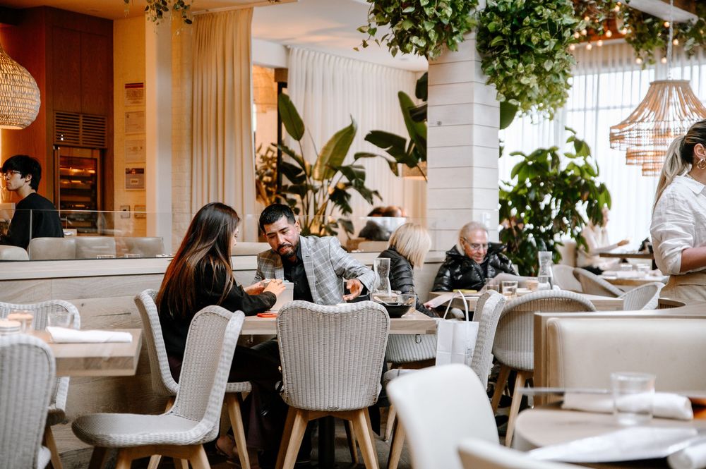 Upscale dining room with comfortable gray chairs and hanging wicker lamps under lush plant decor.