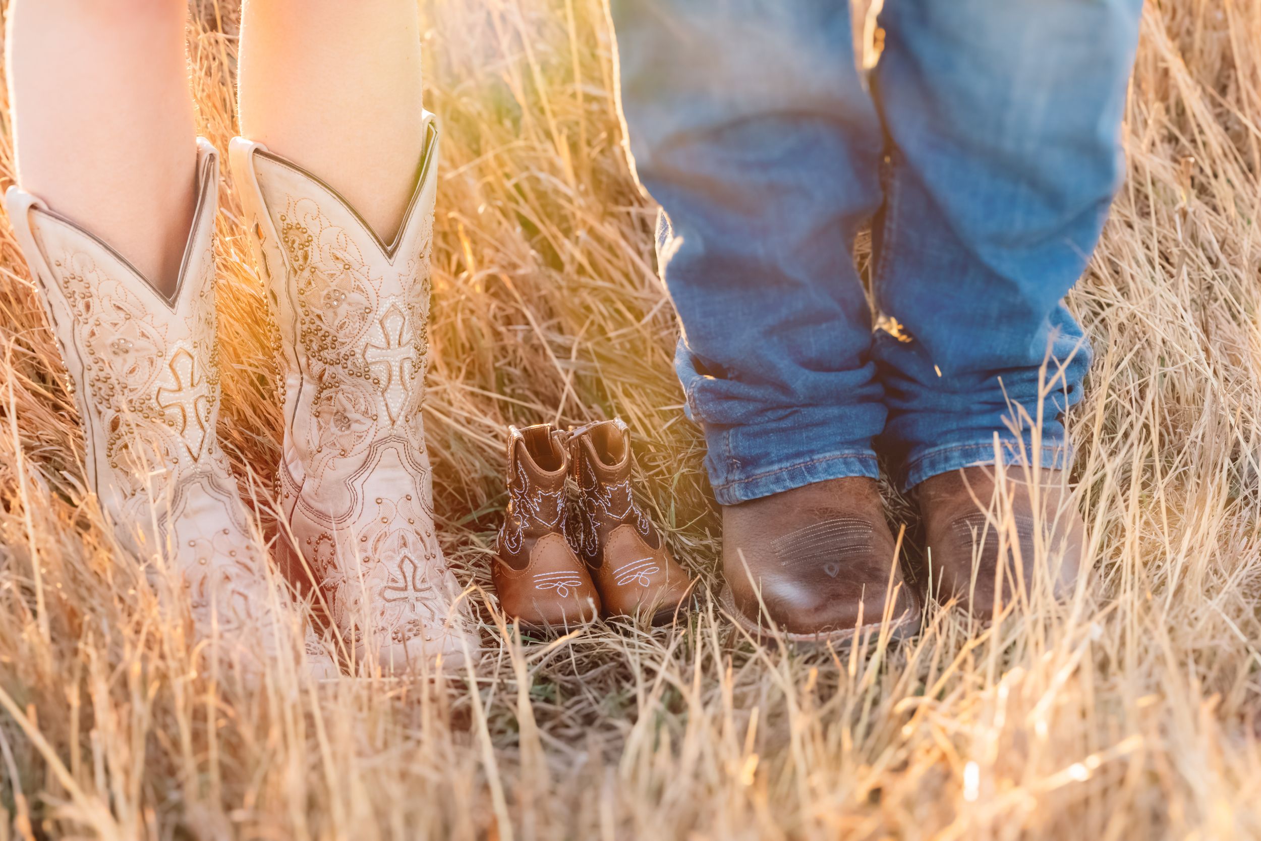 Pair of cowboy boots and boots standing together in tall golden grass during sunset.