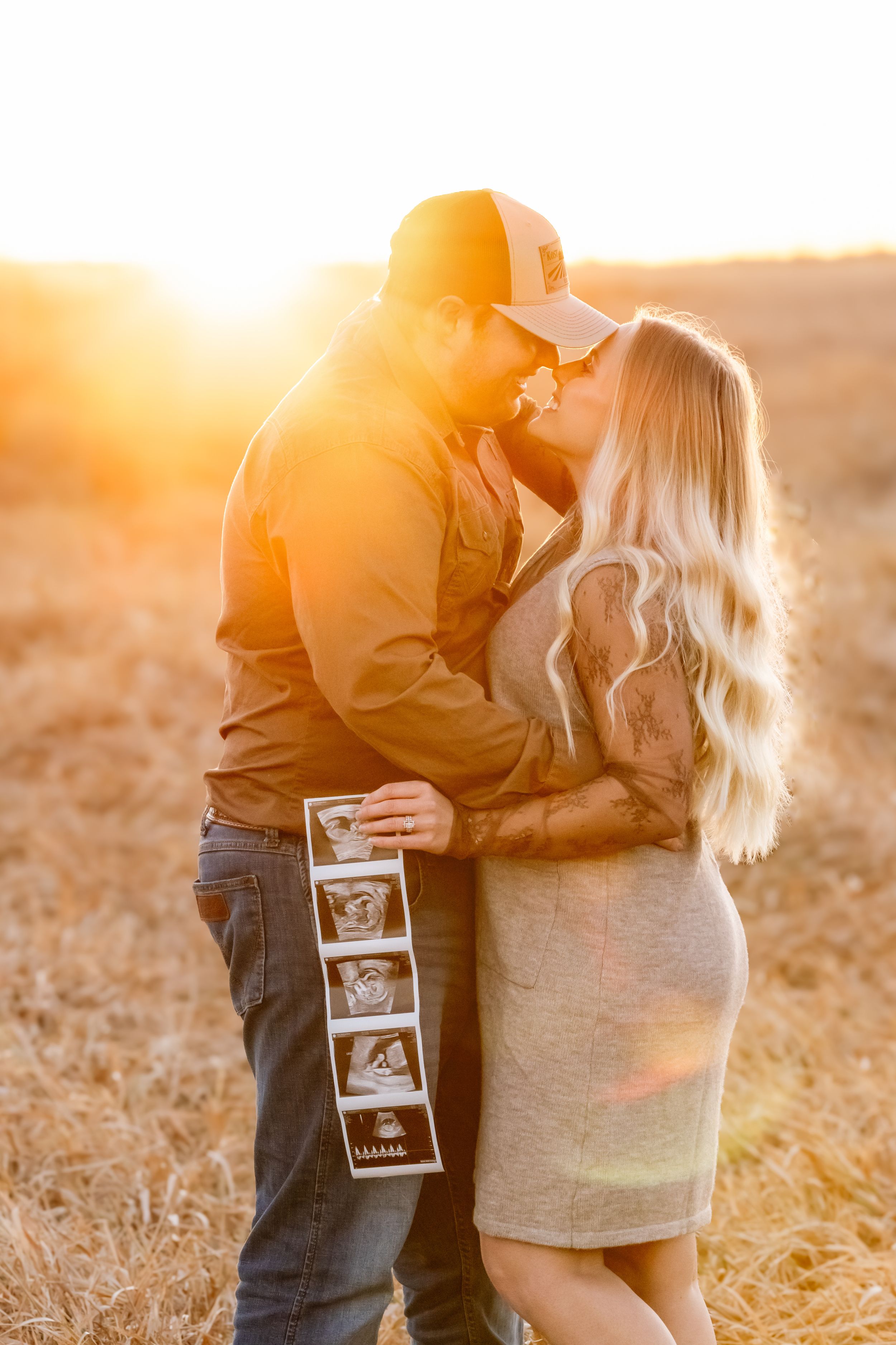 Pregnancy announcement photoshoot with ultrasound images held in golden sunset light.