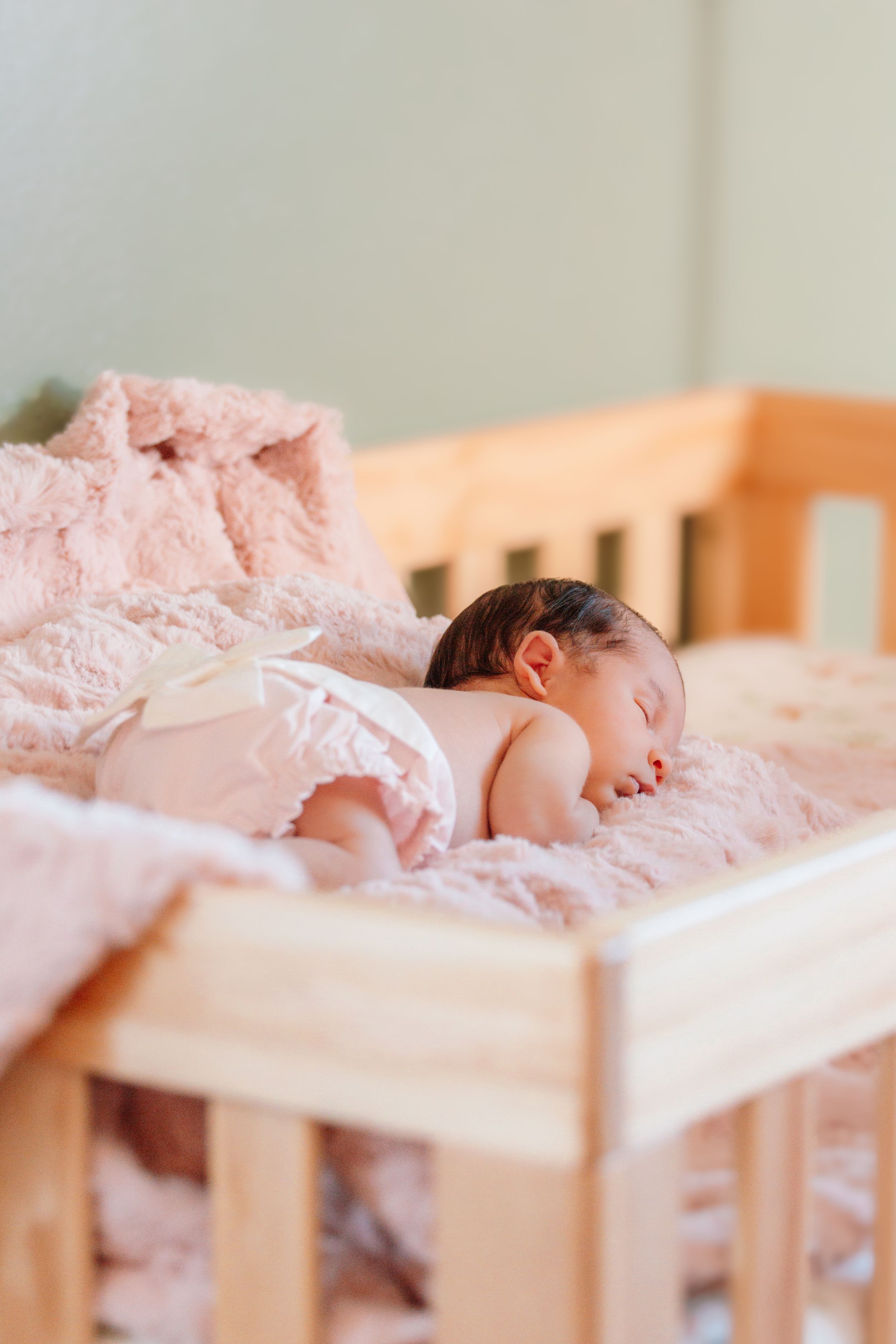 A sleeping baby lies peacefully in a wooden crib with soft pink blankets.