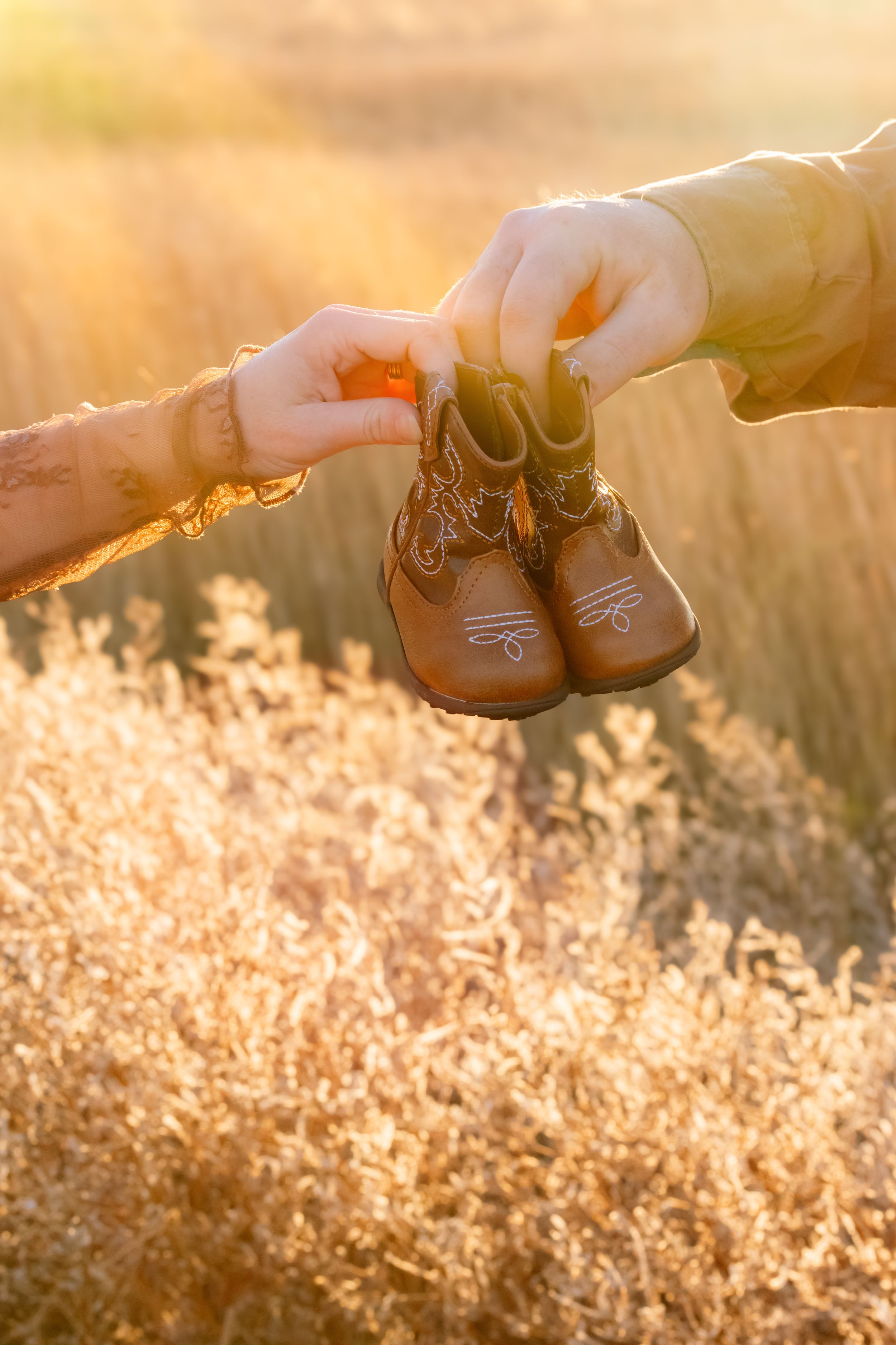 Two hands reach toward each other during golden hour sunlight in a grassy field.