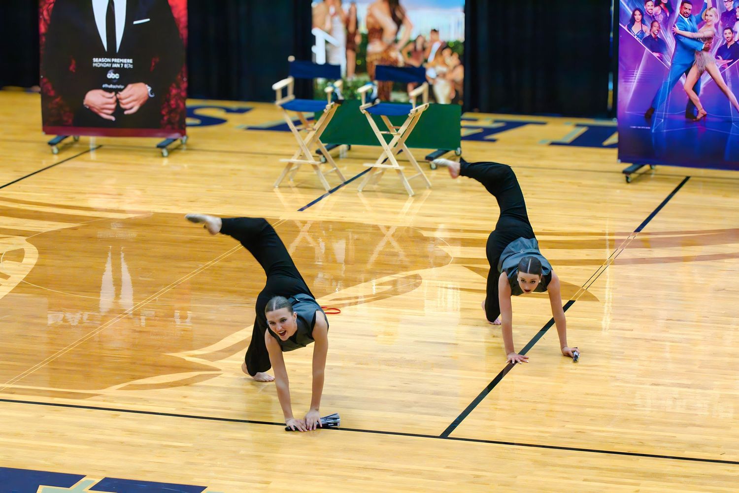 Street dancer executing a dynamic floor routine with aerial moves on a wooden basketball court.