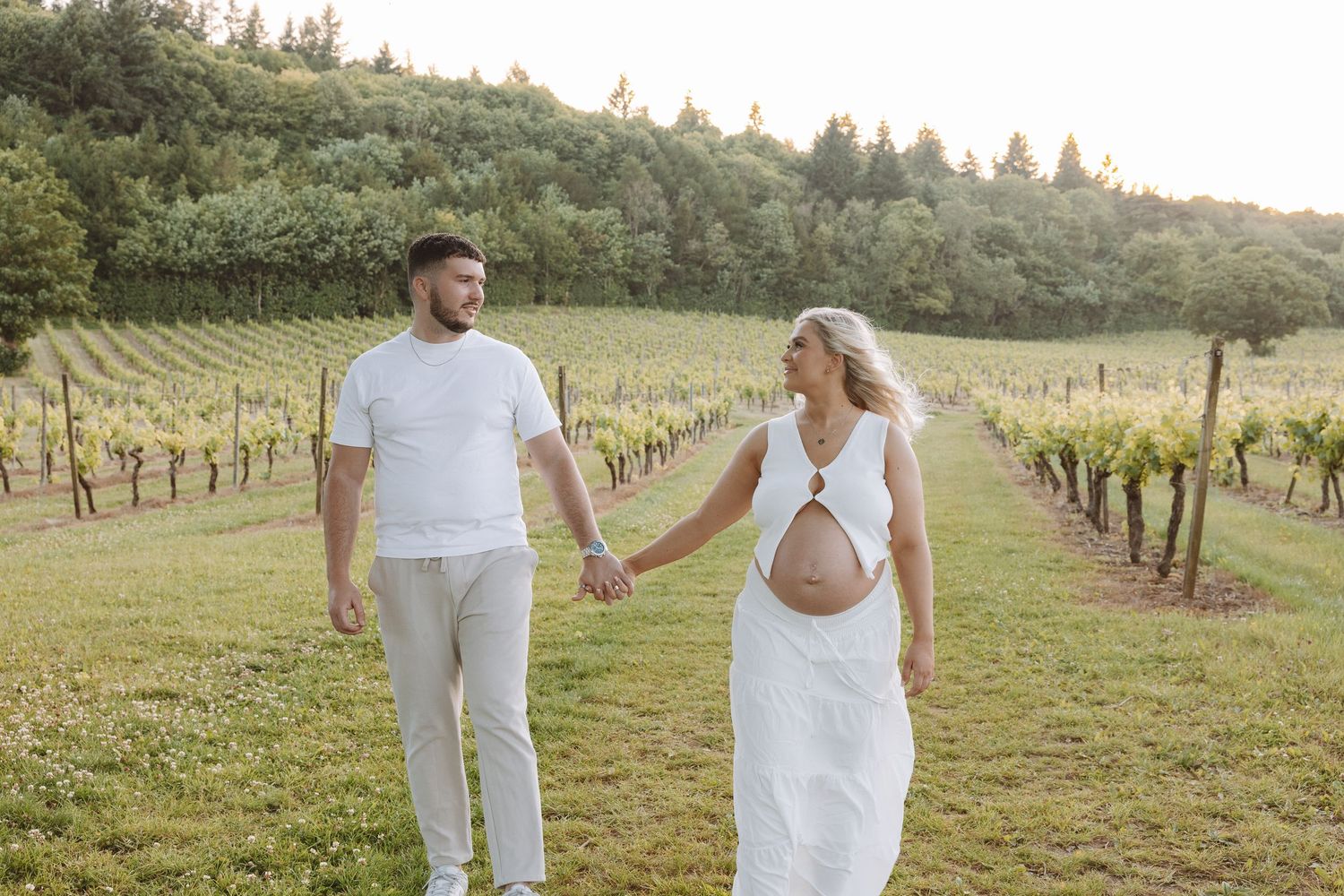 People walk together hand in hand through a scenic vineyard on a sunny afternoon.