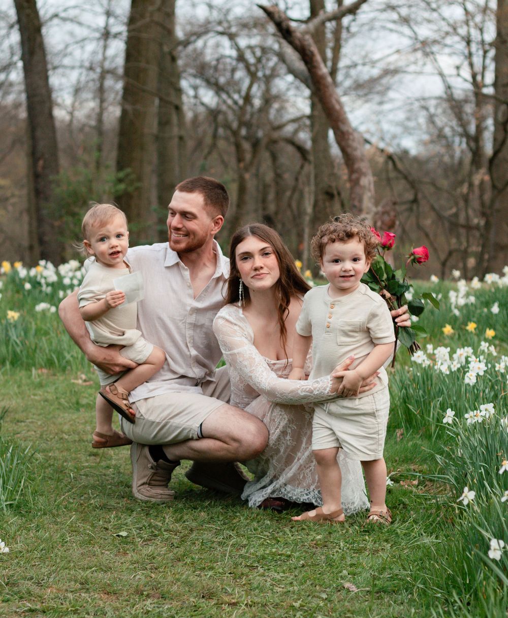 A family poses together in a spring garden with blooming white daffodils visible along the edge of the grass.