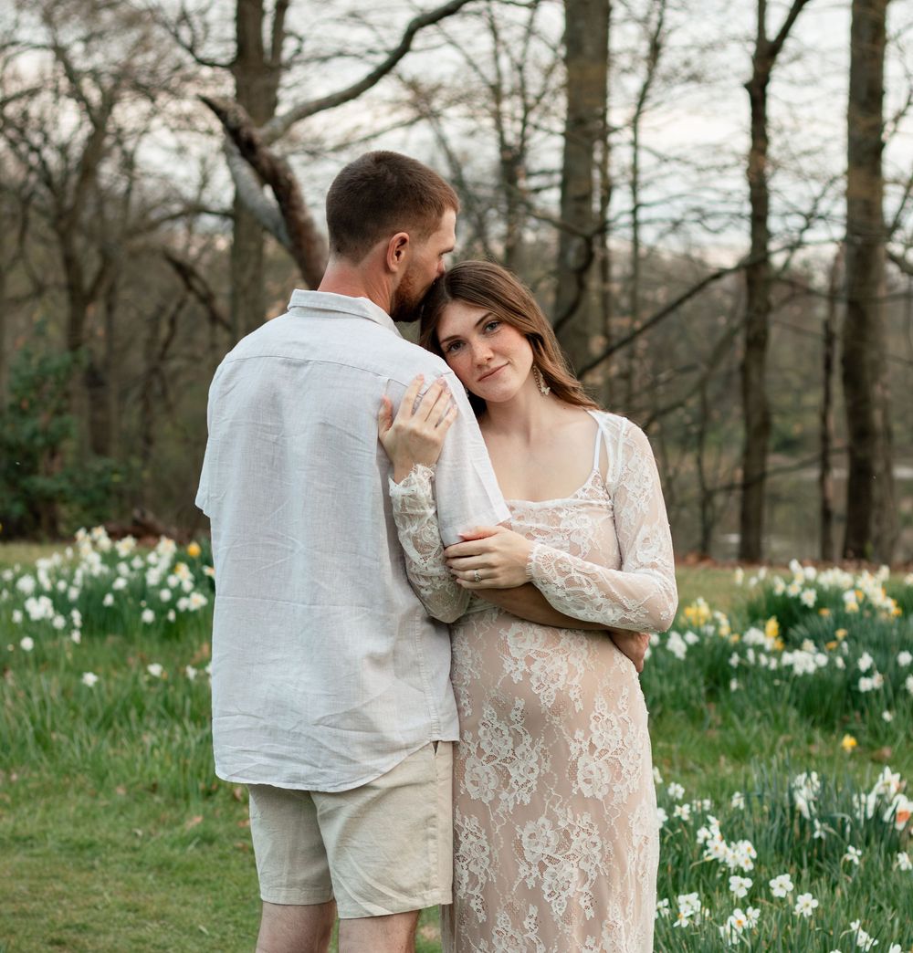 Romantic couple embraces in springtime meadow surrounded by blooming white daffodils in a wooded setting.