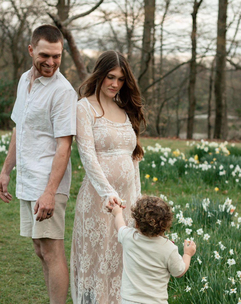 A family stands together in a field of blooming daffodils during springtime at sunset.