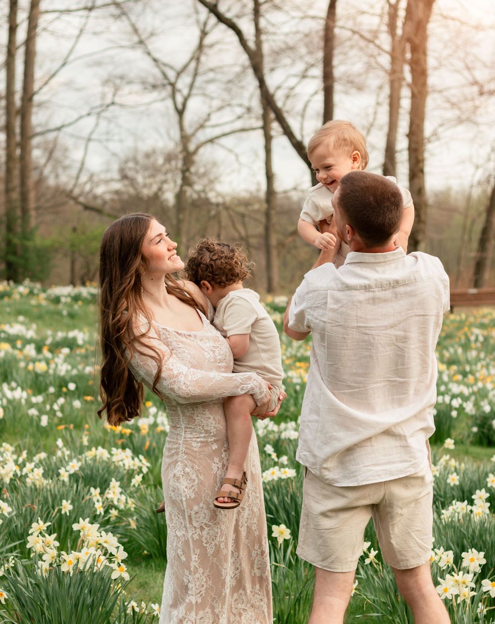 A mother in a lace dress spins and dances with her child in a spring garden filled with blooming daffodils.