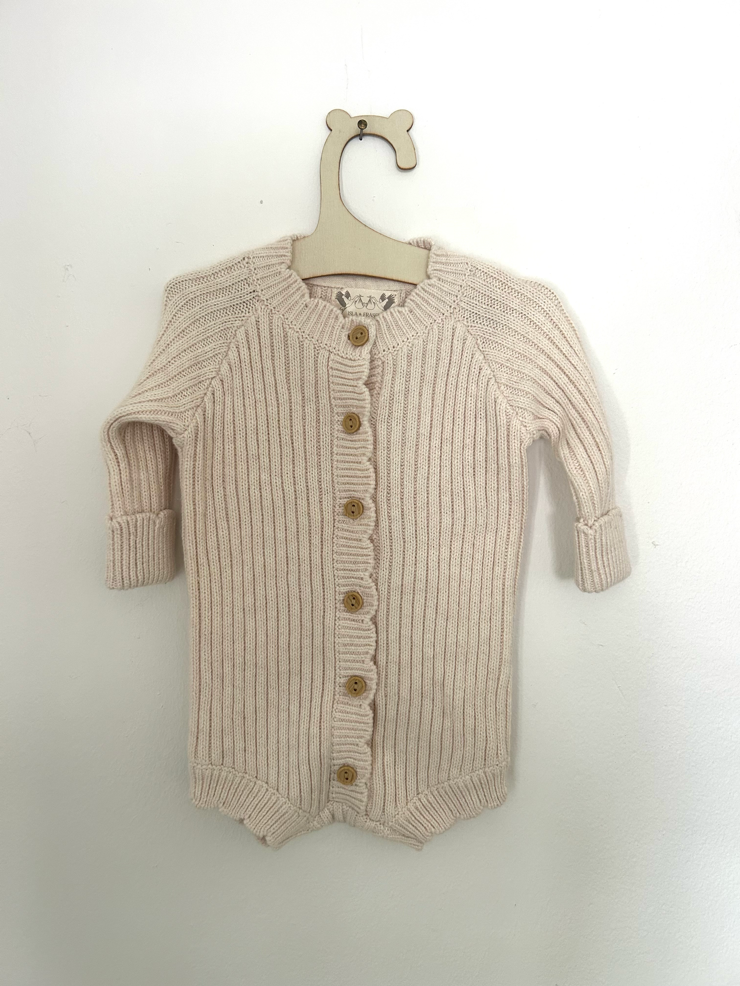 Vintage-style beige knitted baby romper with button details and side pockets hanging on display.