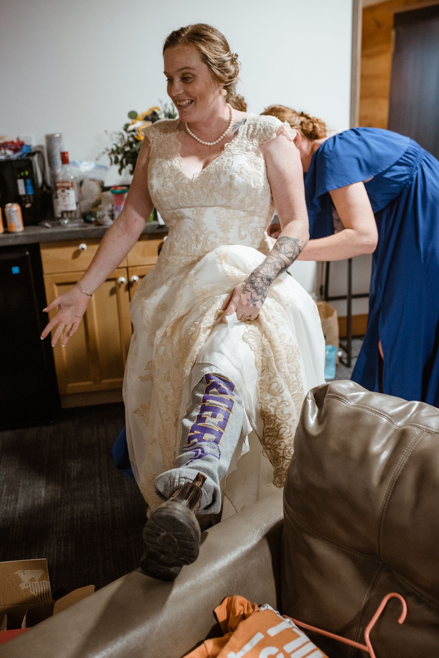 Someone in a lace wedding dress shows off purple sneakers while getting ready in a kitchen setting.