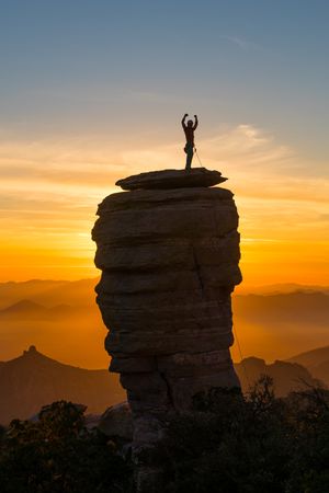 Silhouette of a person on a rocky outcrop against vibrant orange mountain sunset in Chiricahua National Monument.