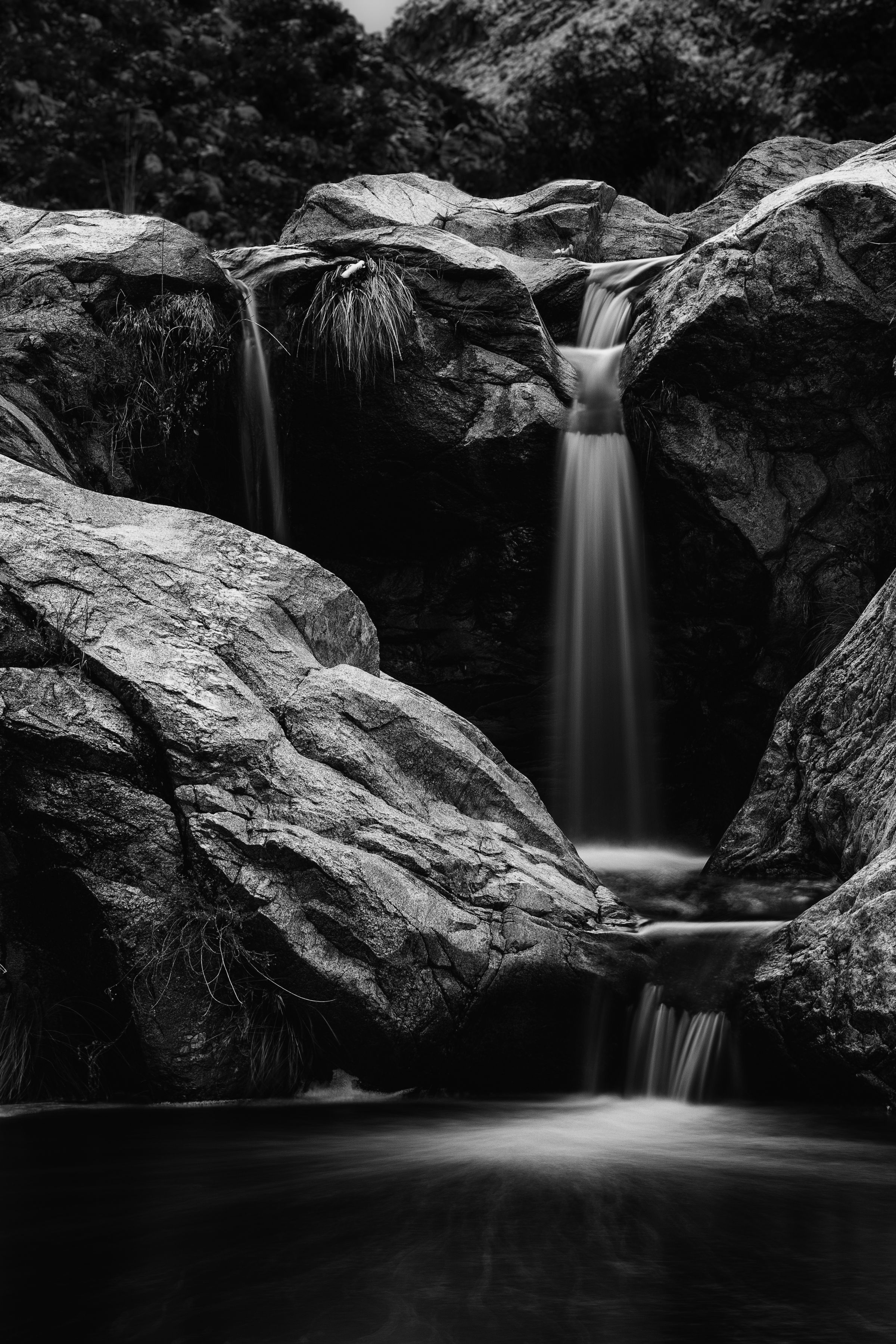 A series of black and white waterfall photographs showing smooth cascading water flowing between dramatic rocky outcrops.