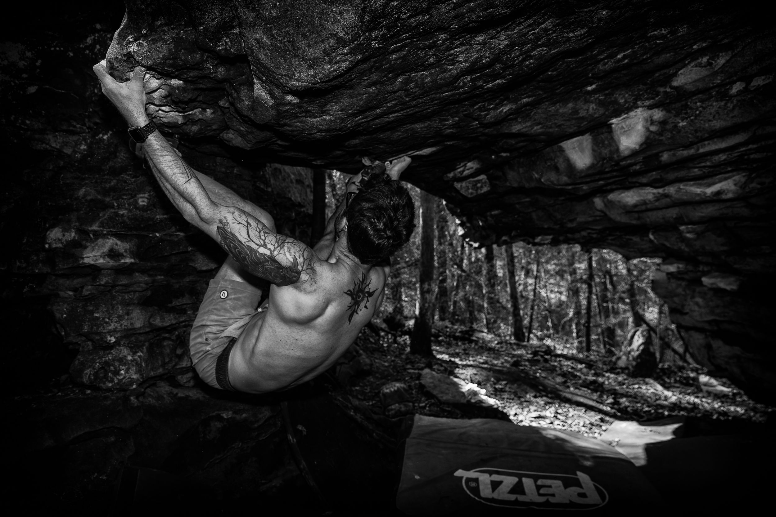 Rock climber performs a difficult overhang move while bouldering in dramatic black and white lighting.