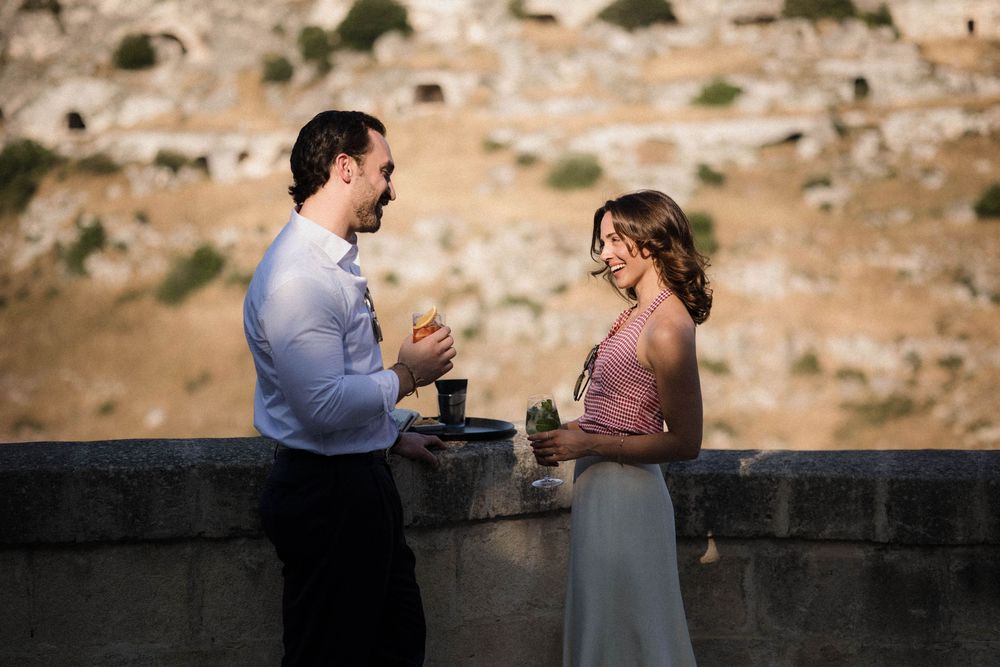 Two people sharing an intimate conversation on a rooftop terrace overlooking an ancient Mediterranean hillside town.