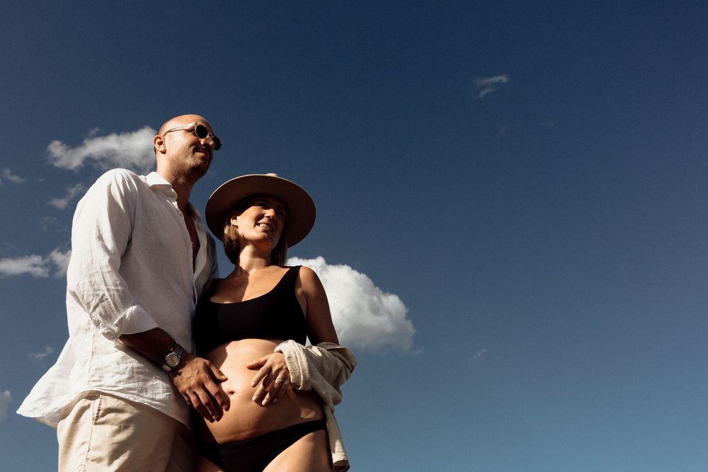 A couple embraces against a dramatic blue sky with clouds during a romantic outdoor photo shoot.