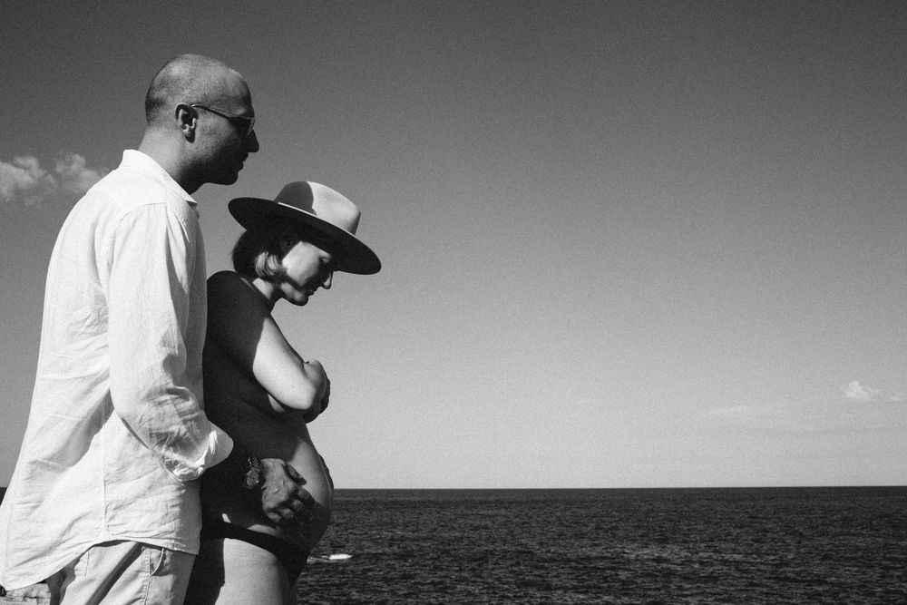 Black and white photo of a couple embracing by the ocean under a cloudy sky.