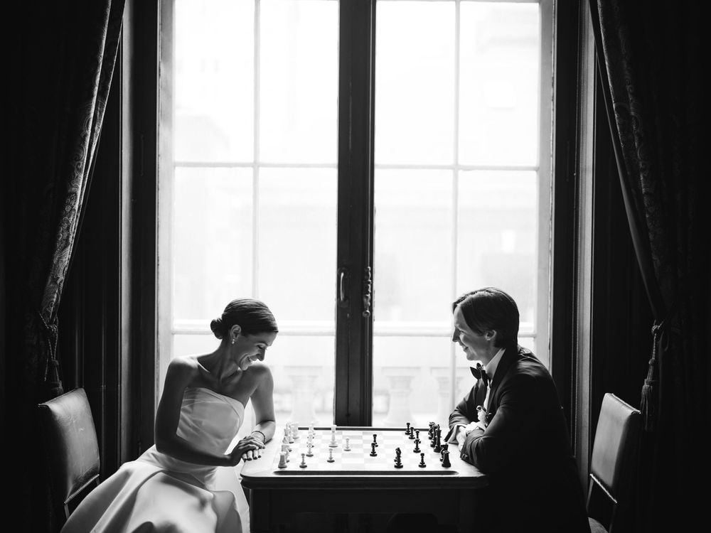 Stylish couple plays chess by the window at the Union League in Philadelphia — a timeless wedding moment full of elegance and charm.