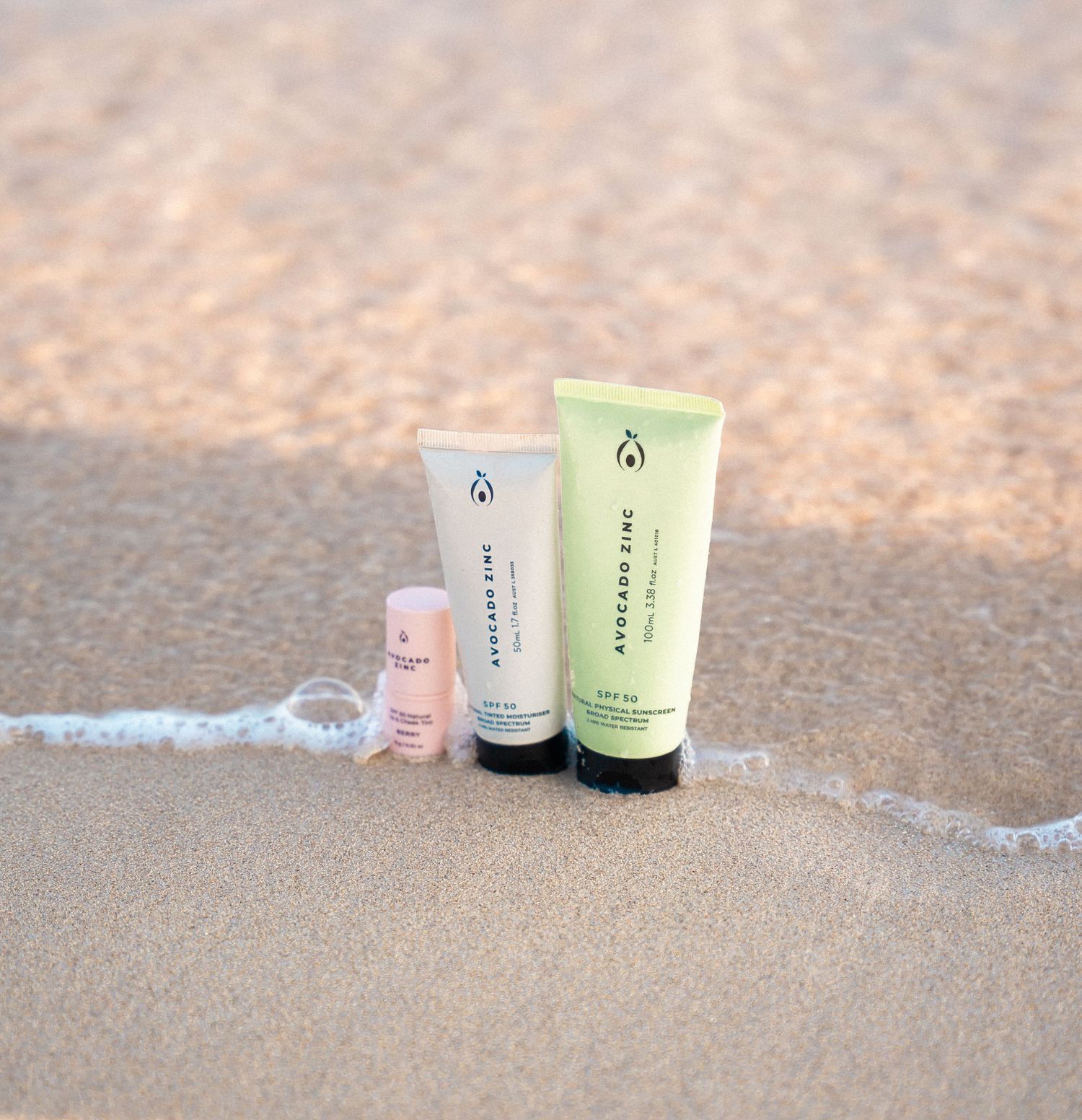 Three skincare product tubes arranged on wet sand with ocean wave.