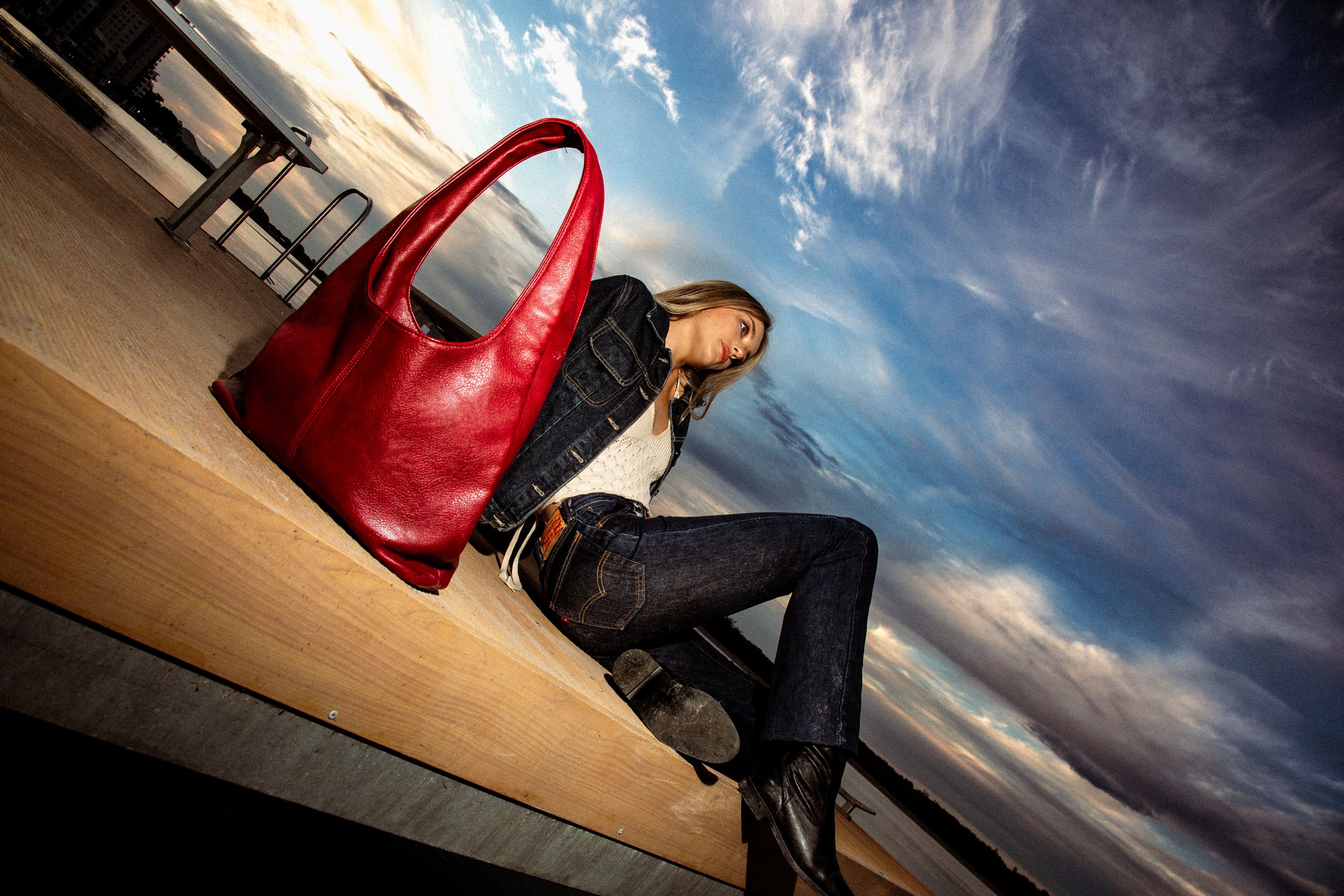 Fashion shoot with a bright red handbag against dramatic evening sky on a wooden deck.