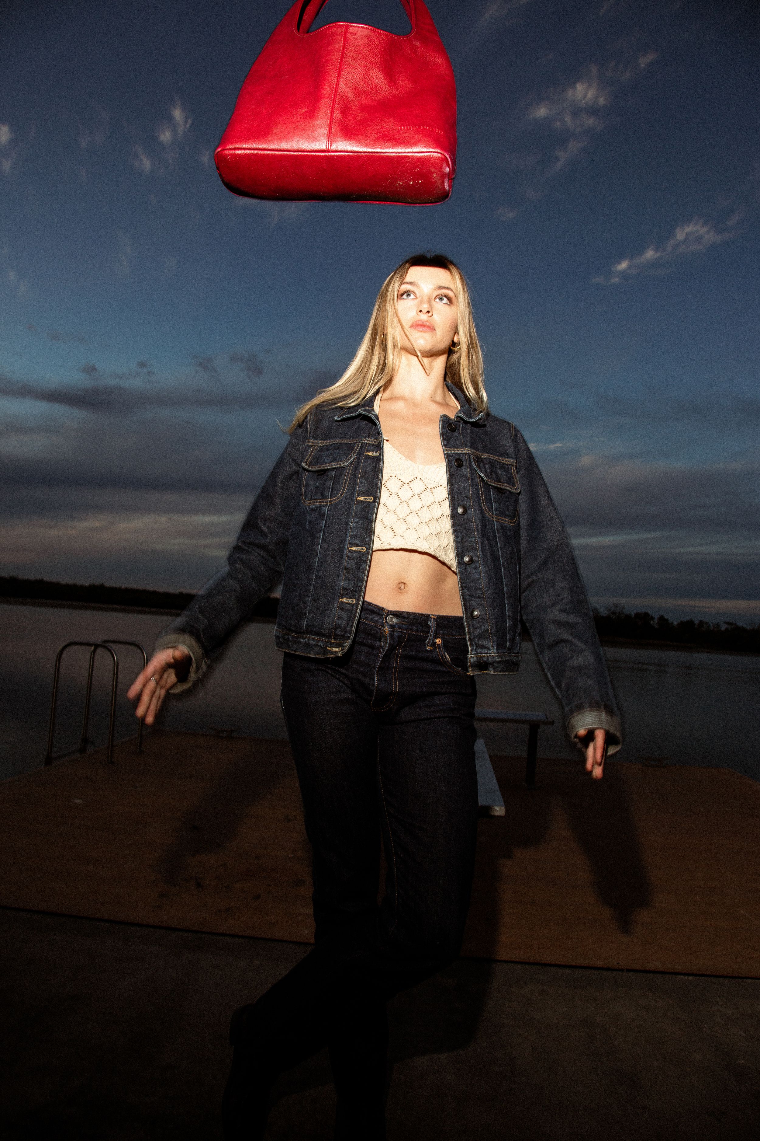 Person in denim jacket with red leather beret poses in moody sunset lighting for fashion editorial series.