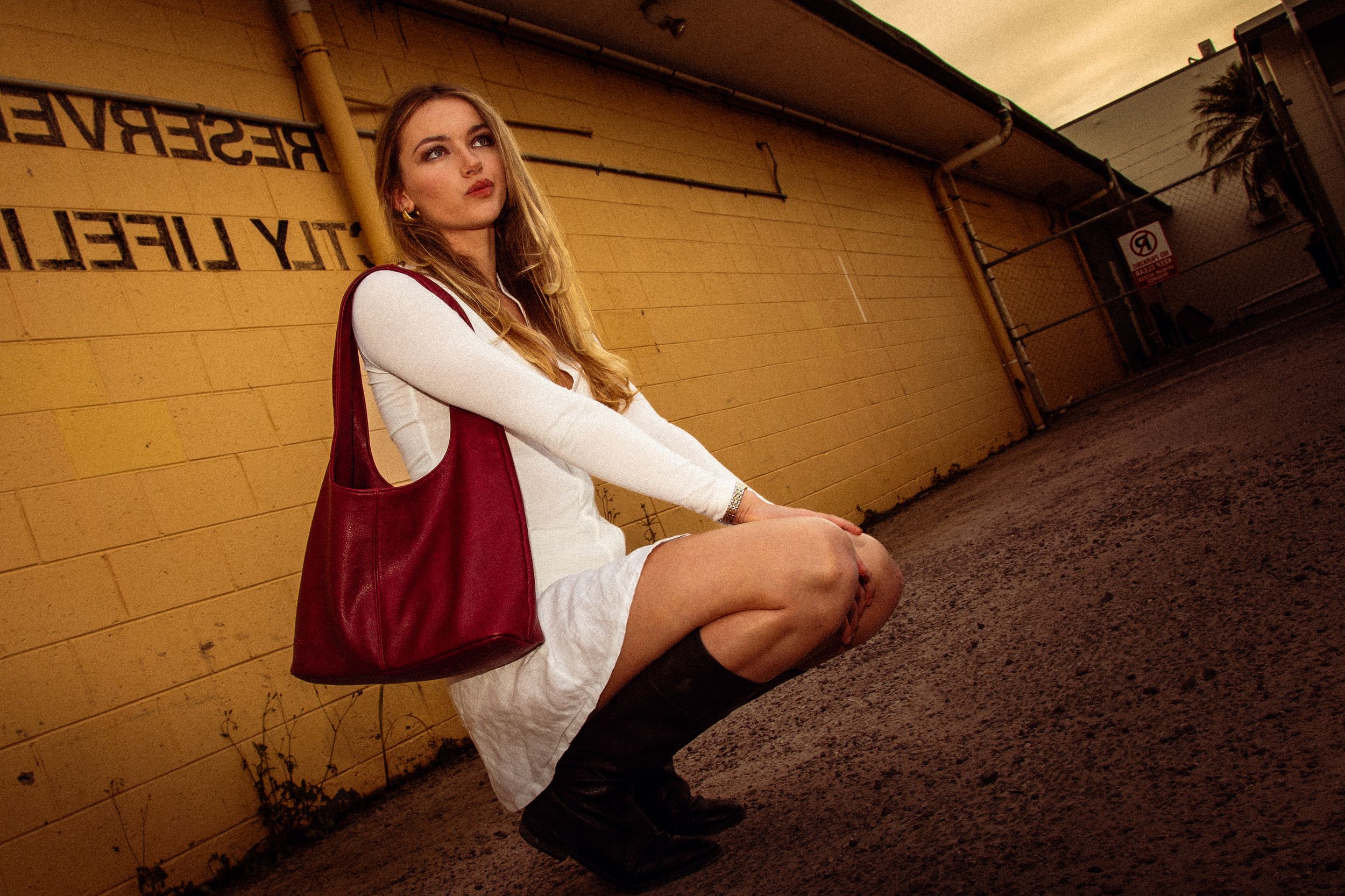 Person in burgundy knit dress and boots strikes a pose while leaning against concrete wall in a garage.