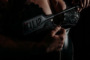A person holds and inspects a black handgun against a dark background with dramatic lighting. Nice & Naughty Store Event Grand Rapids MI
