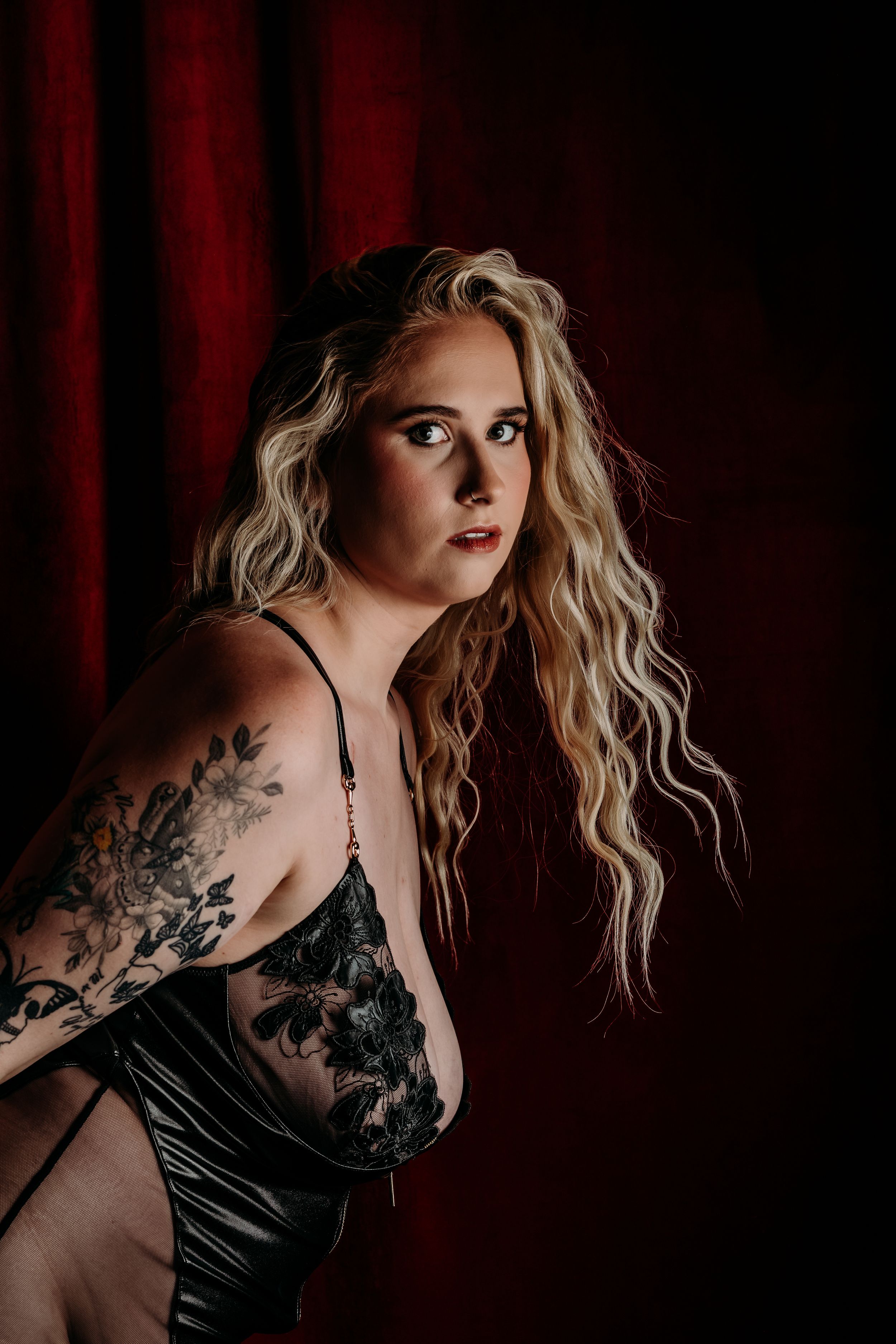 Dramatic boudoir portrait with blonde wavy hair in black lace lingerie against dark red curtain background. grand rapids boudoir Photo, MI