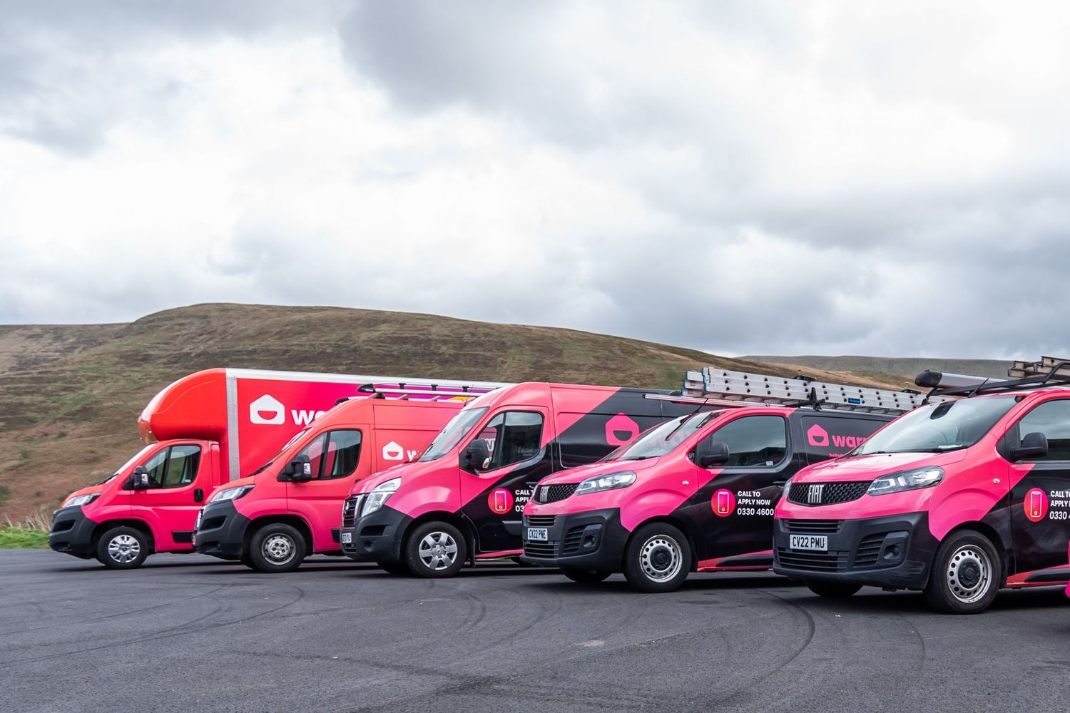 Line of pink commercial vehicles parked in a row against countryside landscape.