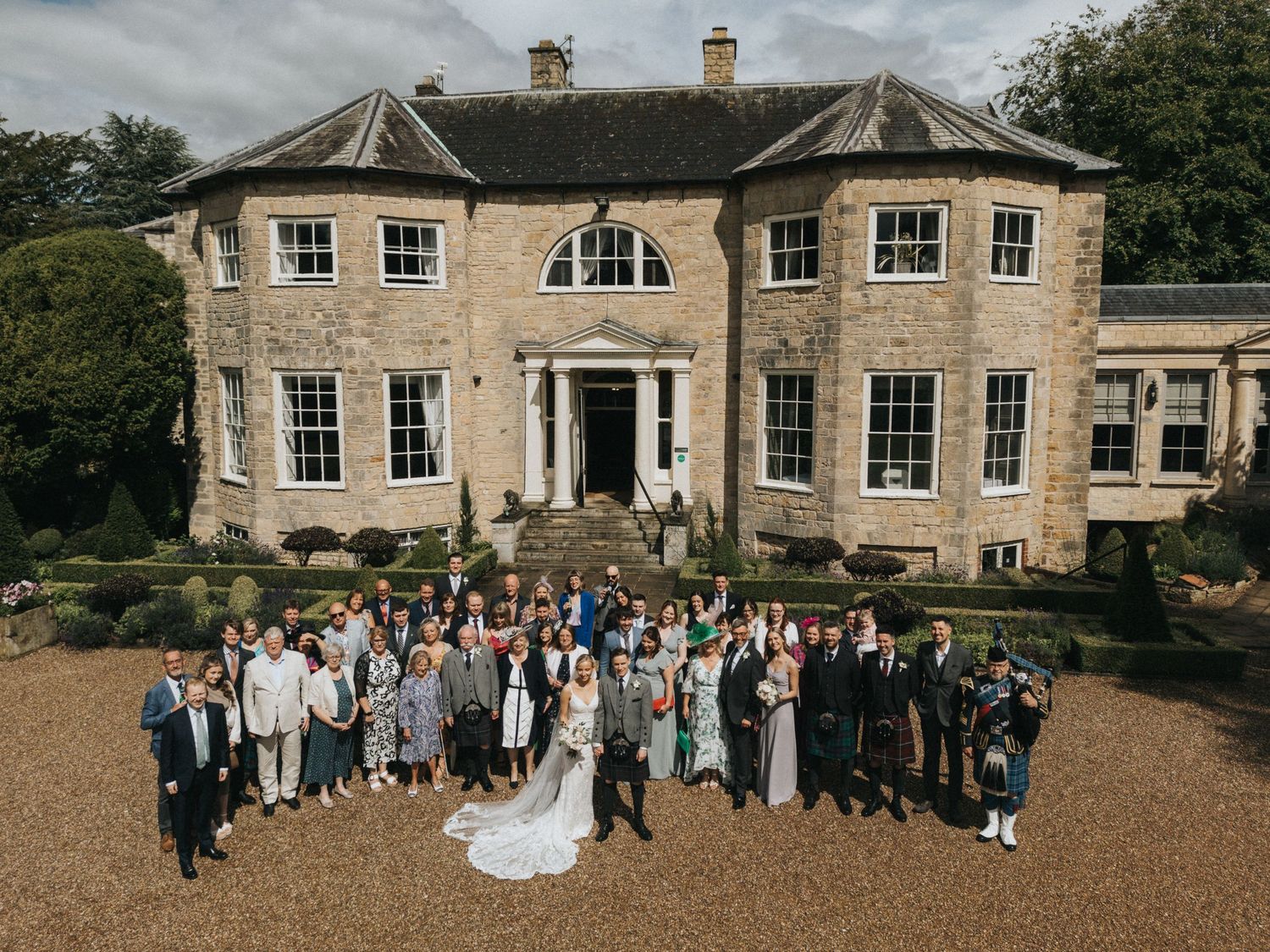 Large group gathered in gravel courtyard for outdoor wedding event in front of Washingborough Hall. Image taken by Grimsby photographers.