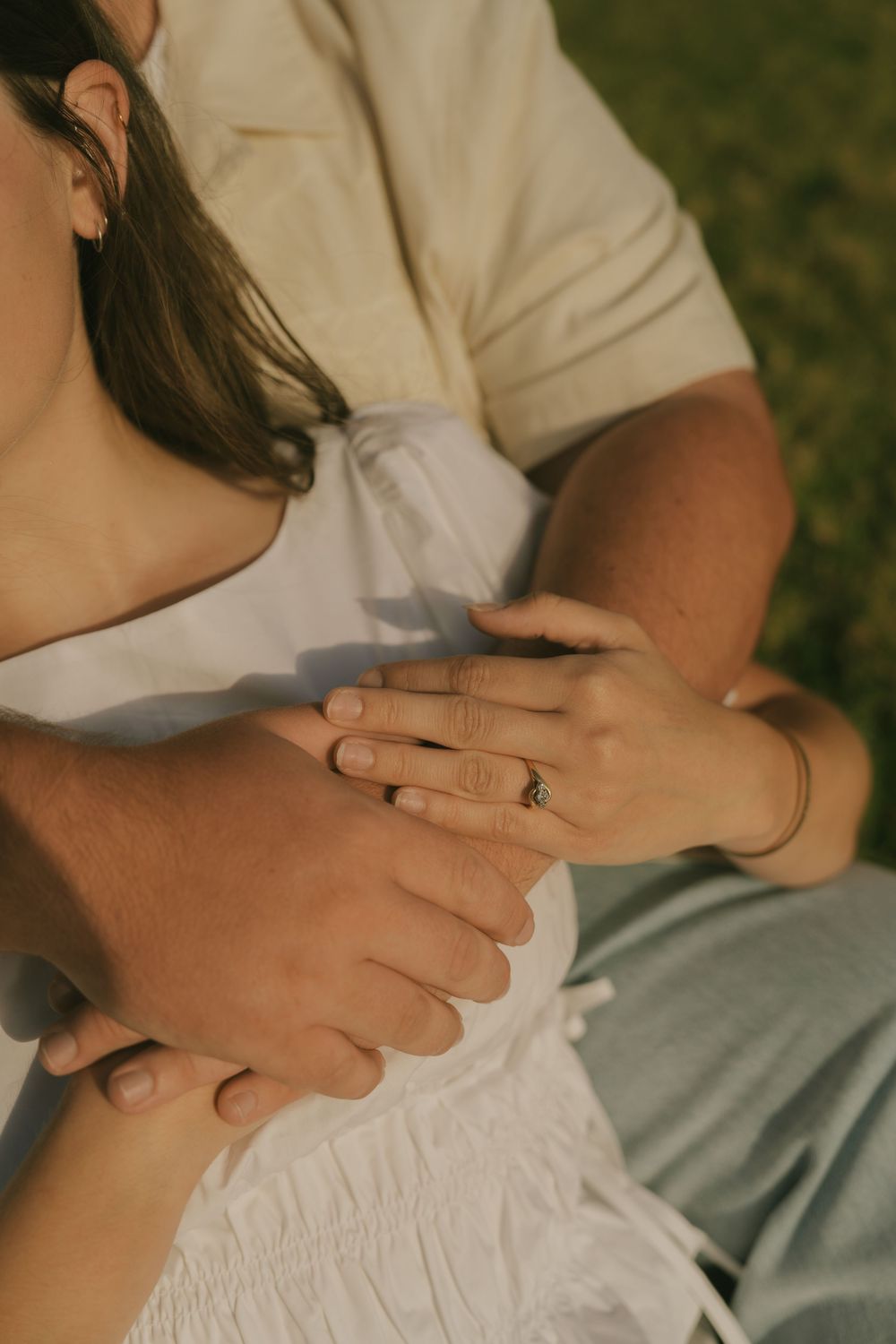 Close-up shot of hands with wedding rings embracing in warm sunlight.