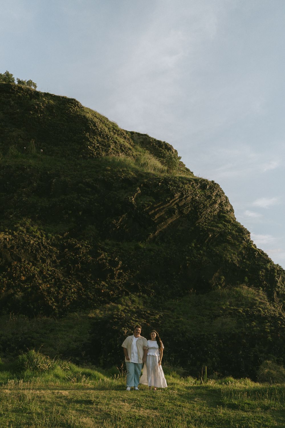 Two people in white outfits walking along a scenic coastal hillside at sunset.