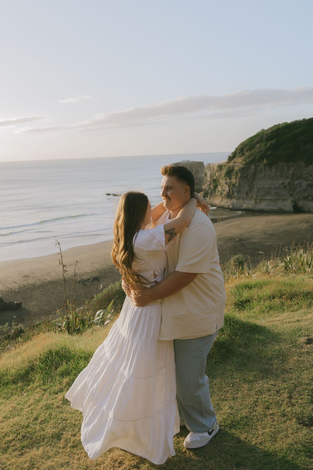 A romantic couple in white clothing dancing on a grassy oceanside cliff.