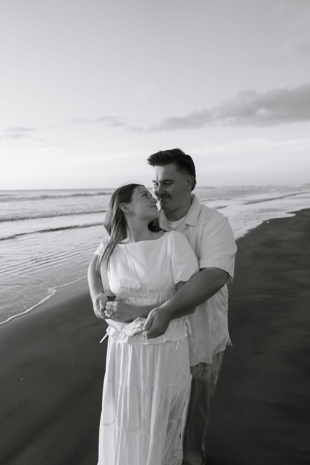 A couple embraces on a black sand beach during sunset.