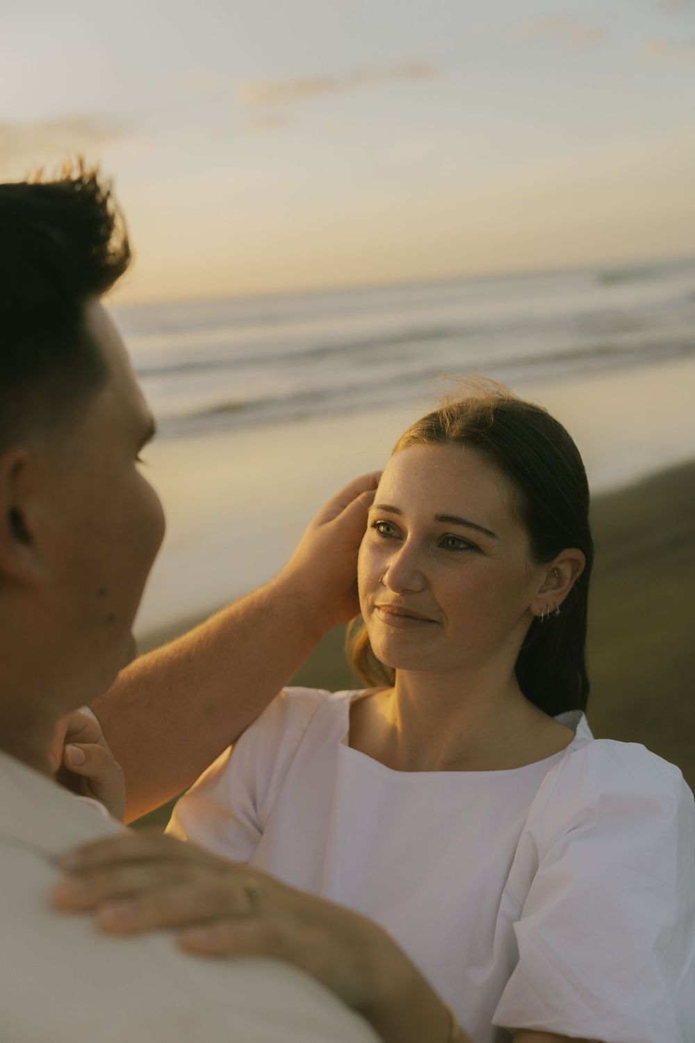 A couple in white clothing shares an intimate moment on the beach at sunset.