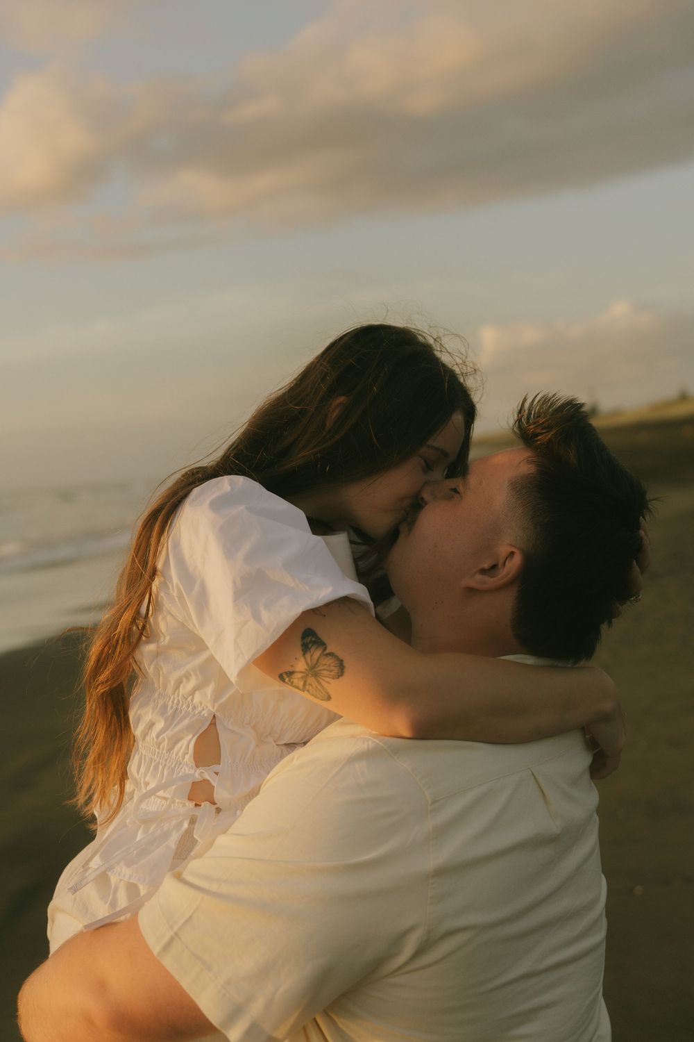 A couple shares an intimate embrace on the beach at golden hour.