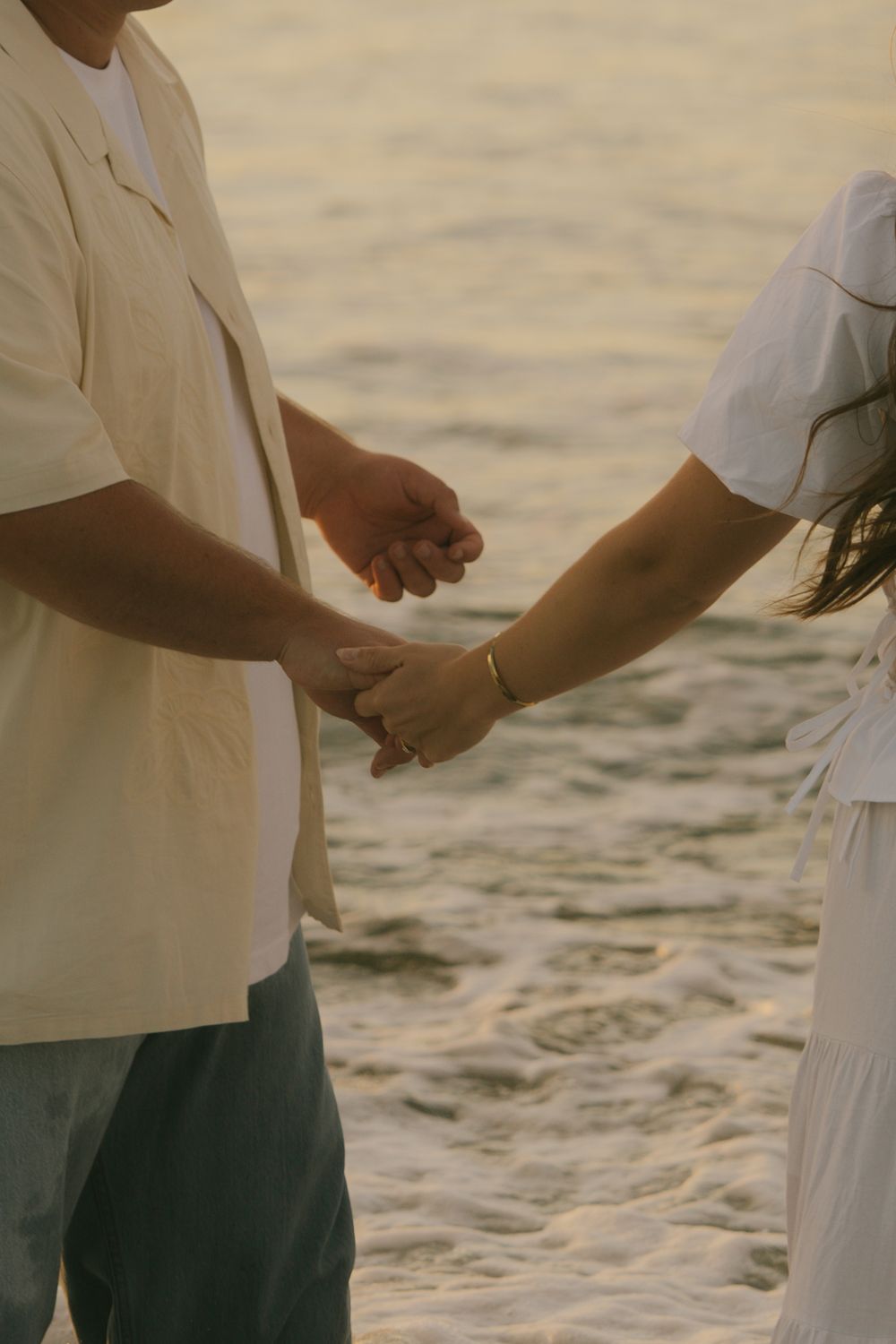 Hands exchanging rings during a beach wedding ceremony at sunset.