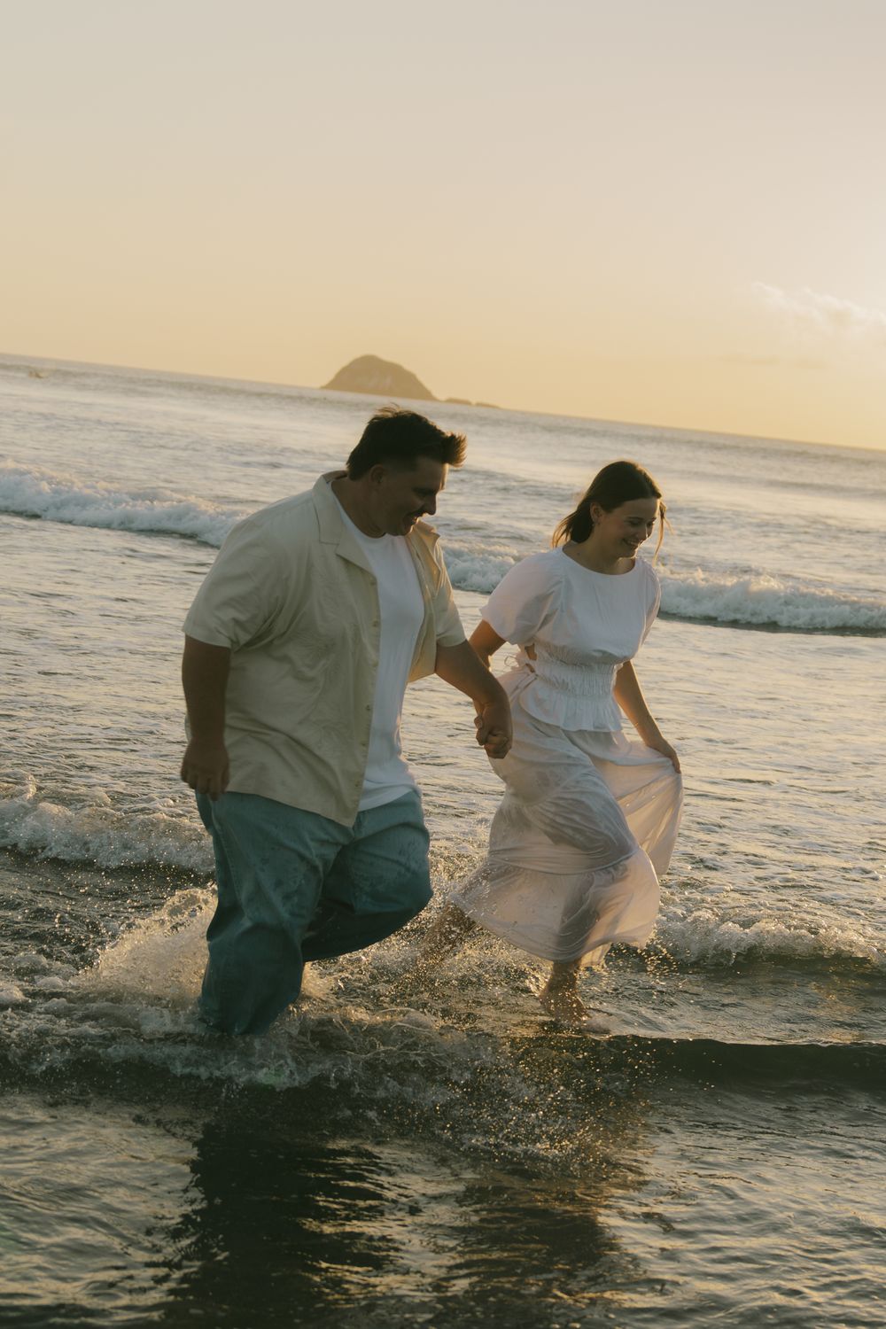 Two people splash and play in the ocean waves during a golden sunset.