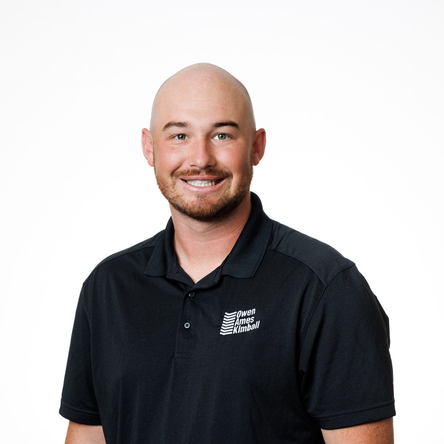 Professional headshot of a person smiling warmly in a black polo shirt with company logo against white background.