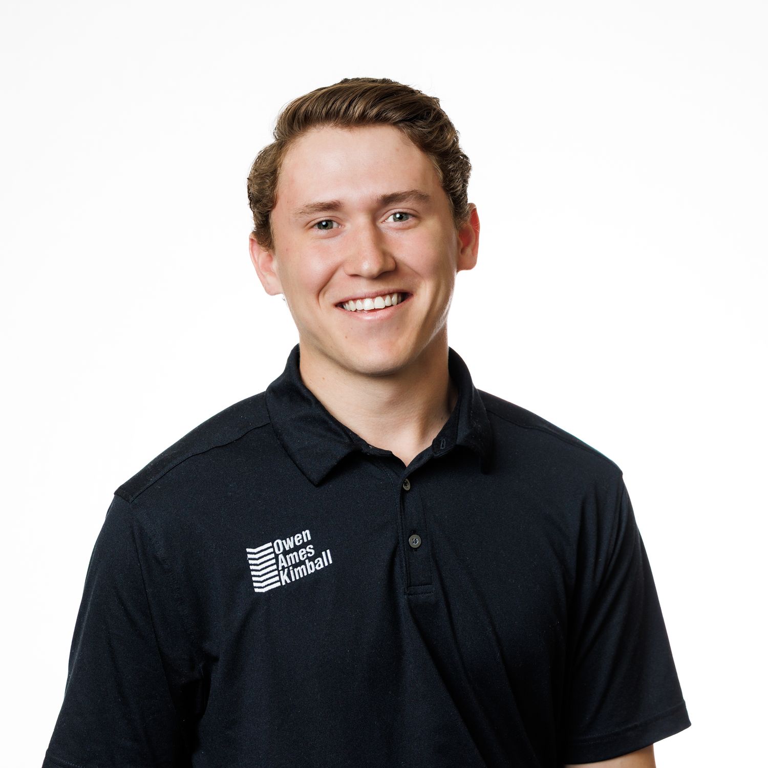 Professional headshot portrait in dark polo shirt with embroidered logo against white background.