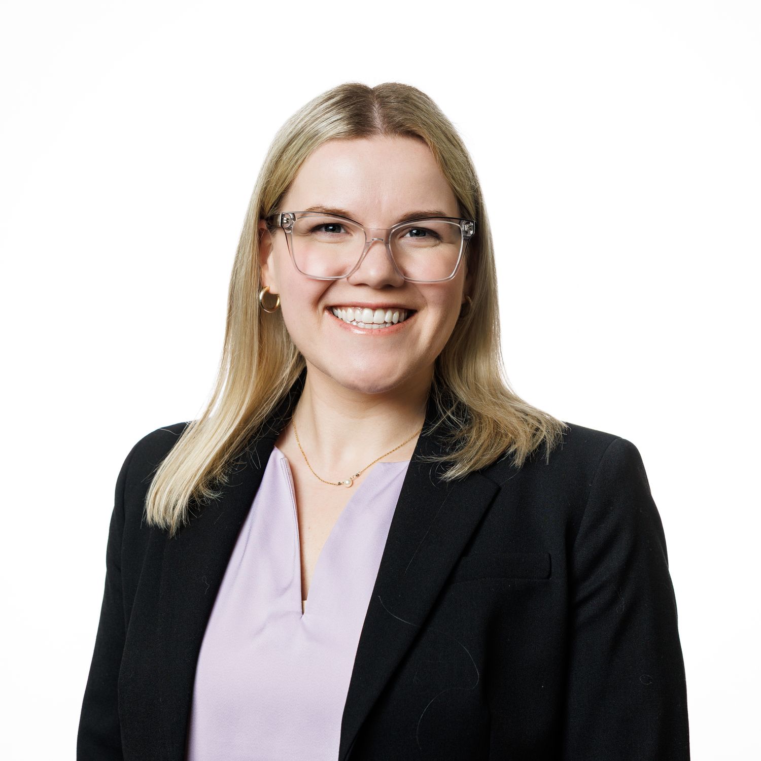 Professional business portrait of person in glasses and black blazer with blonde hair smiling warmly against white background.