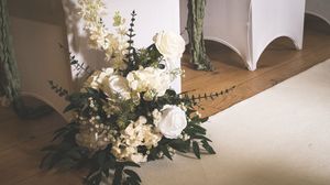 A rustic white floral arrangement with hydrangeas and greenery sits elegantly against a neutral wall.