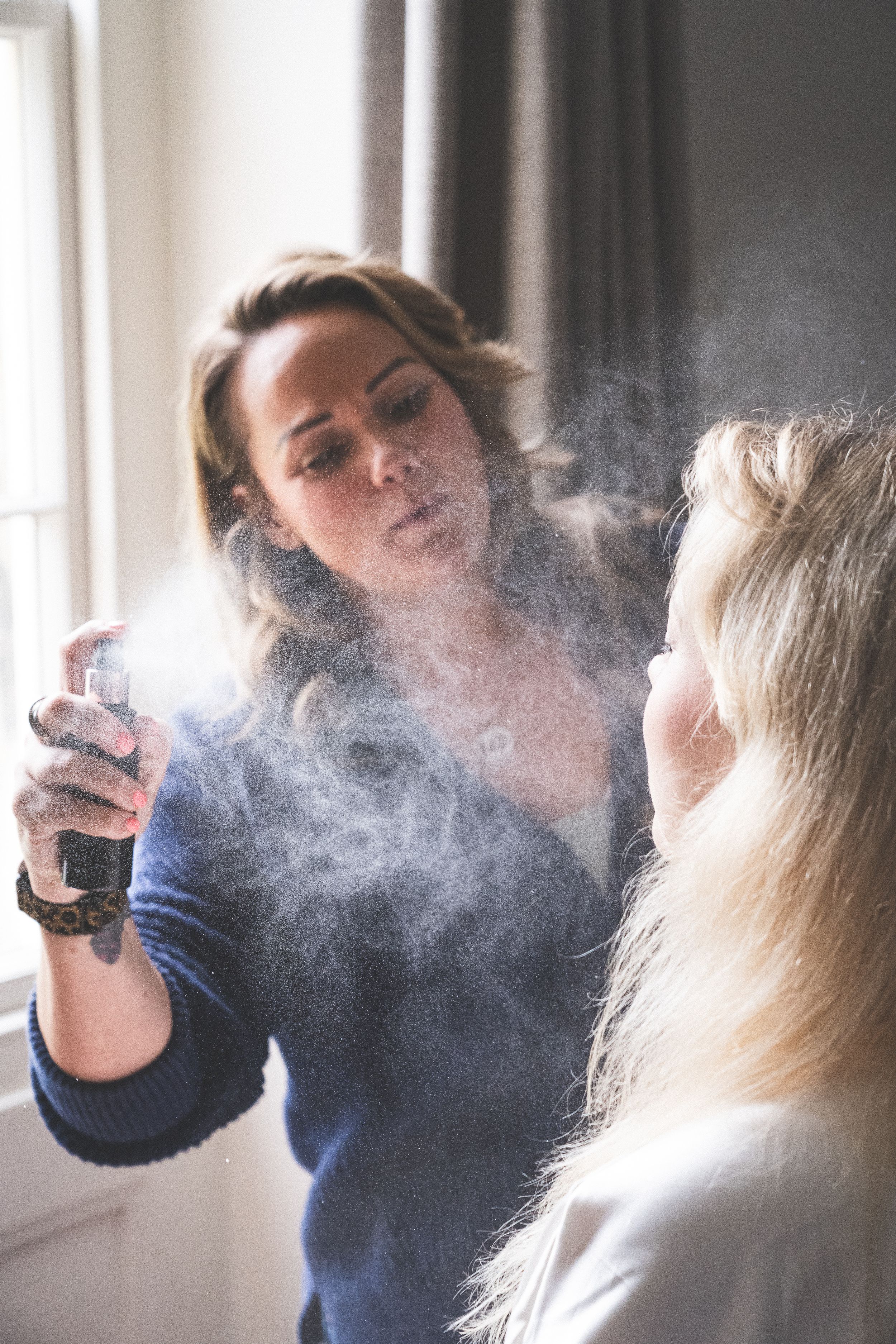 A series of makeup application photos showing hairspray mist being sprayed in soft natural lighting.