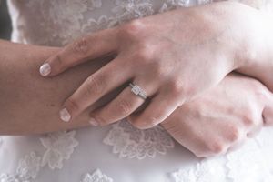 Several hands wearing silver engagement rings and wedding bands shown close up against a white lace background.