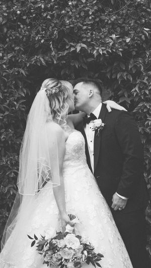 Black and white photo series of a romantic wedding couple in an intimate garden setting with elegant lace gown and trailing veil.