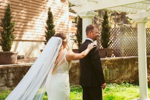 A happy couple in wedding attire sharing a romantic moment under a white outdoor gazebo with greenery.