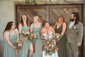 Joyful bridal party in mint green dresses sharing candid laughs against rustic barn door backdrop.